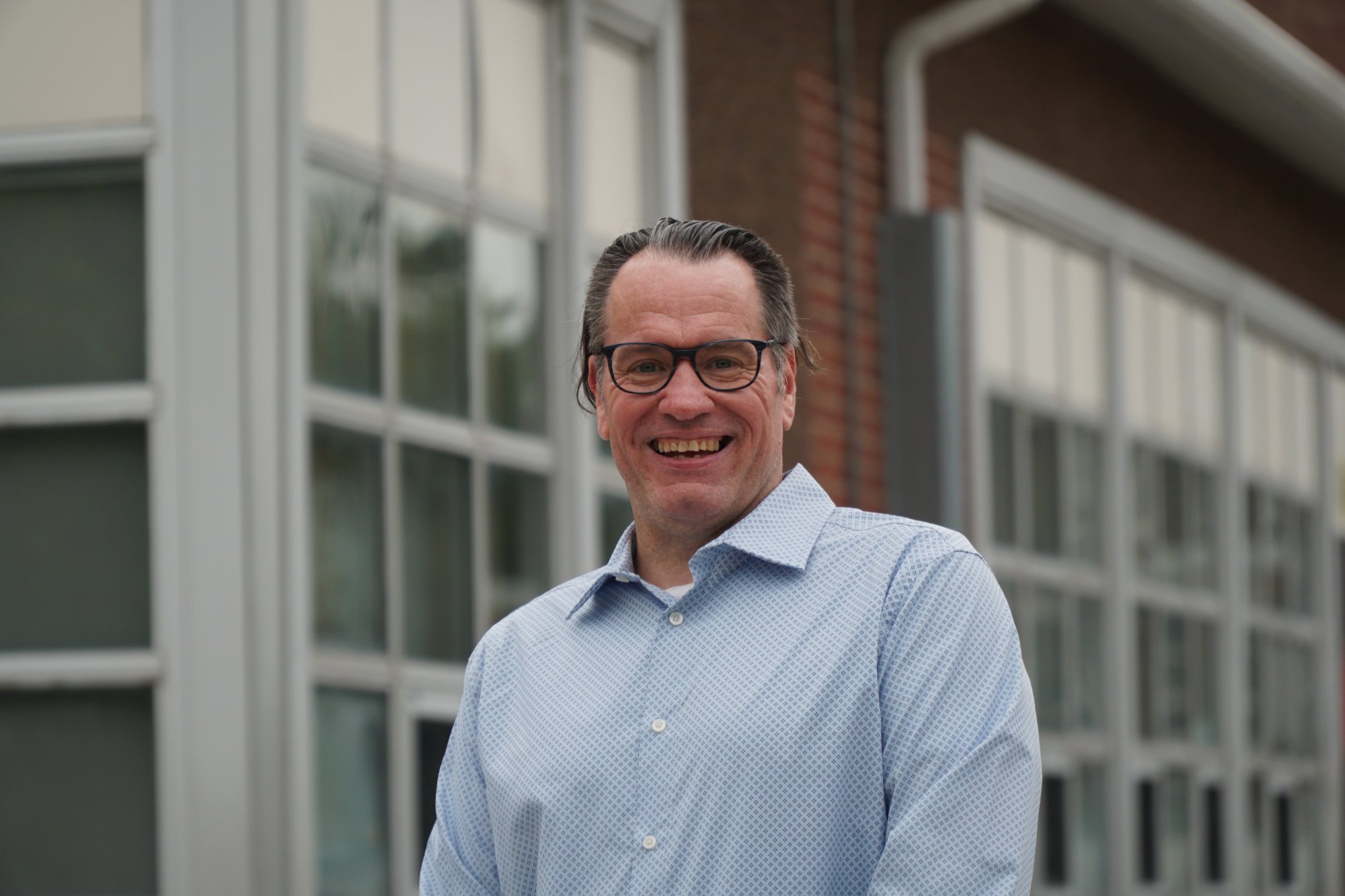 Head-and-shoulders portrait of Glenn Kremp, grey hair tied back, wearing a light blue patterned shirt and glasses.