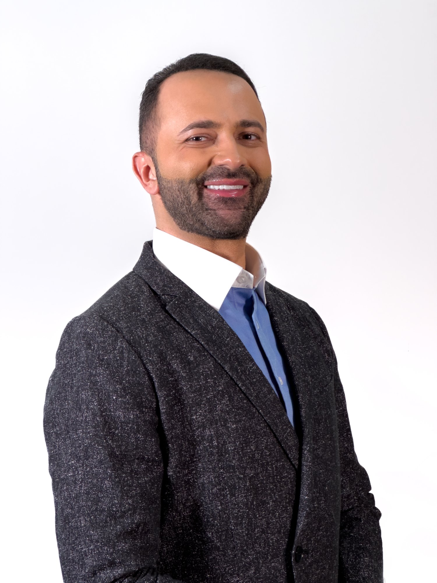 Head-and-shoulders portrait of Nathen Masri, short dark hair and a beard, wearing a dark textured jacket and blue shirt.