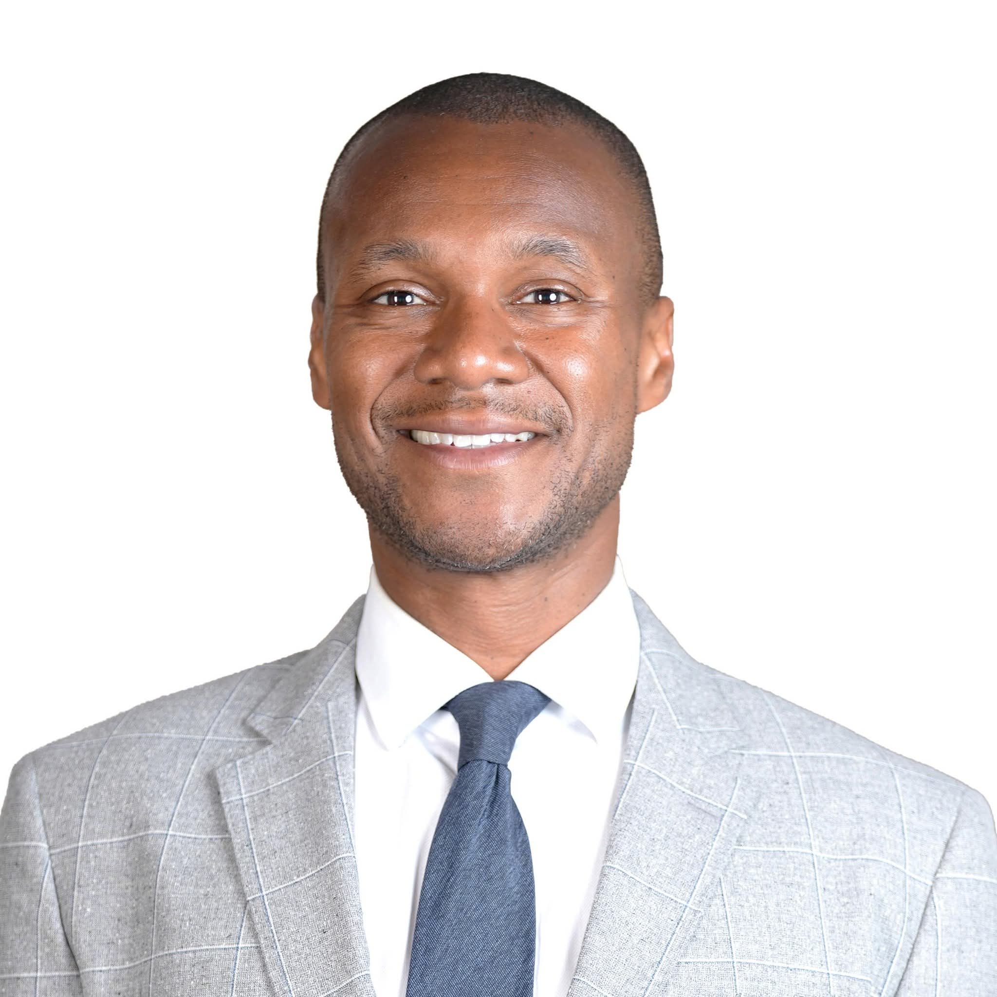 Head-and-shoulders portrait of Jamaal Myers, short dark hair and light stubble, wearing a grey checked blazer, white shirt, and blue tie.
