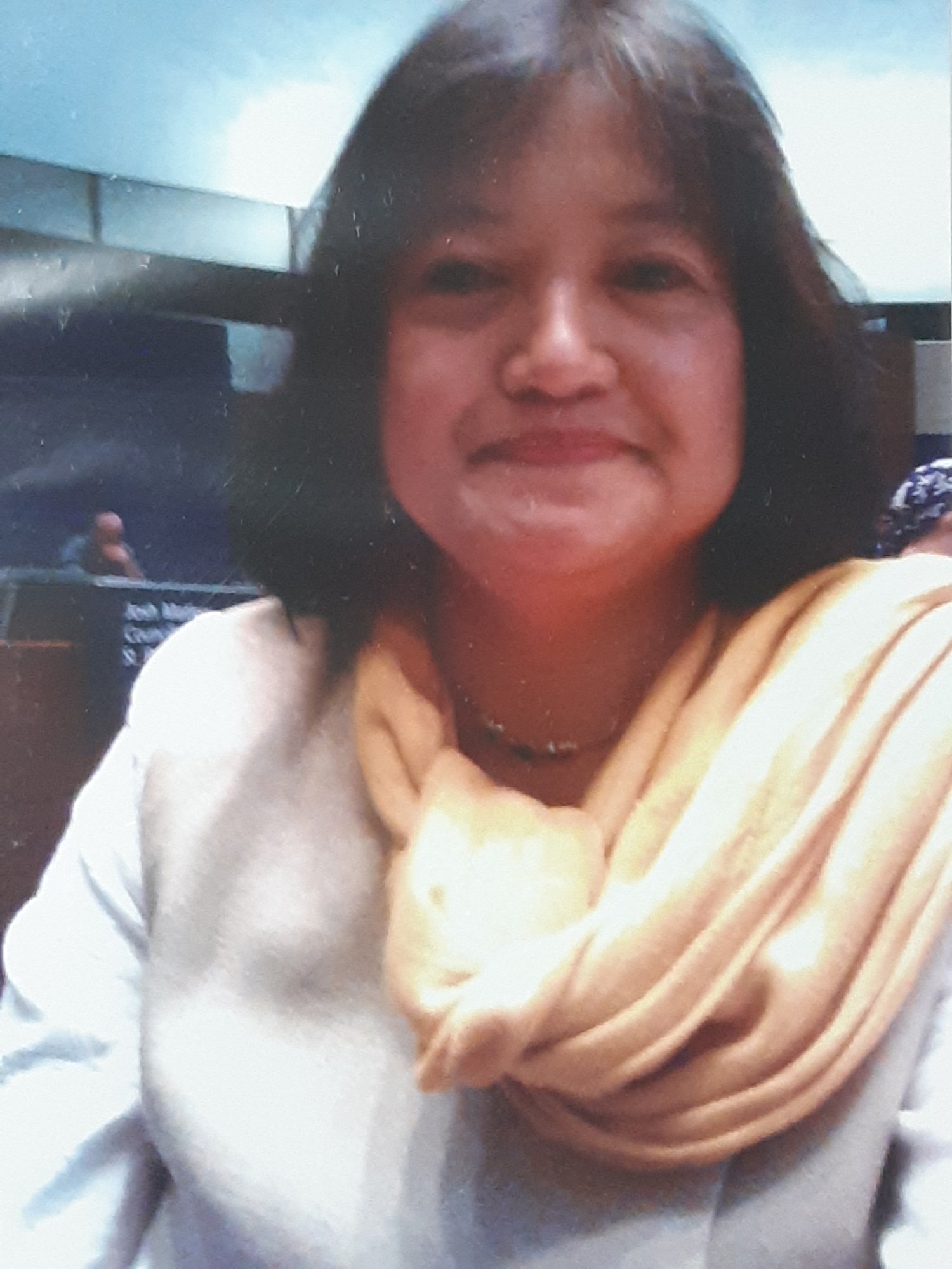 Head-and-shoulders portrait of Aria Garcia, shoulder-length dark hair, wearing a white top and a yellow scarf.