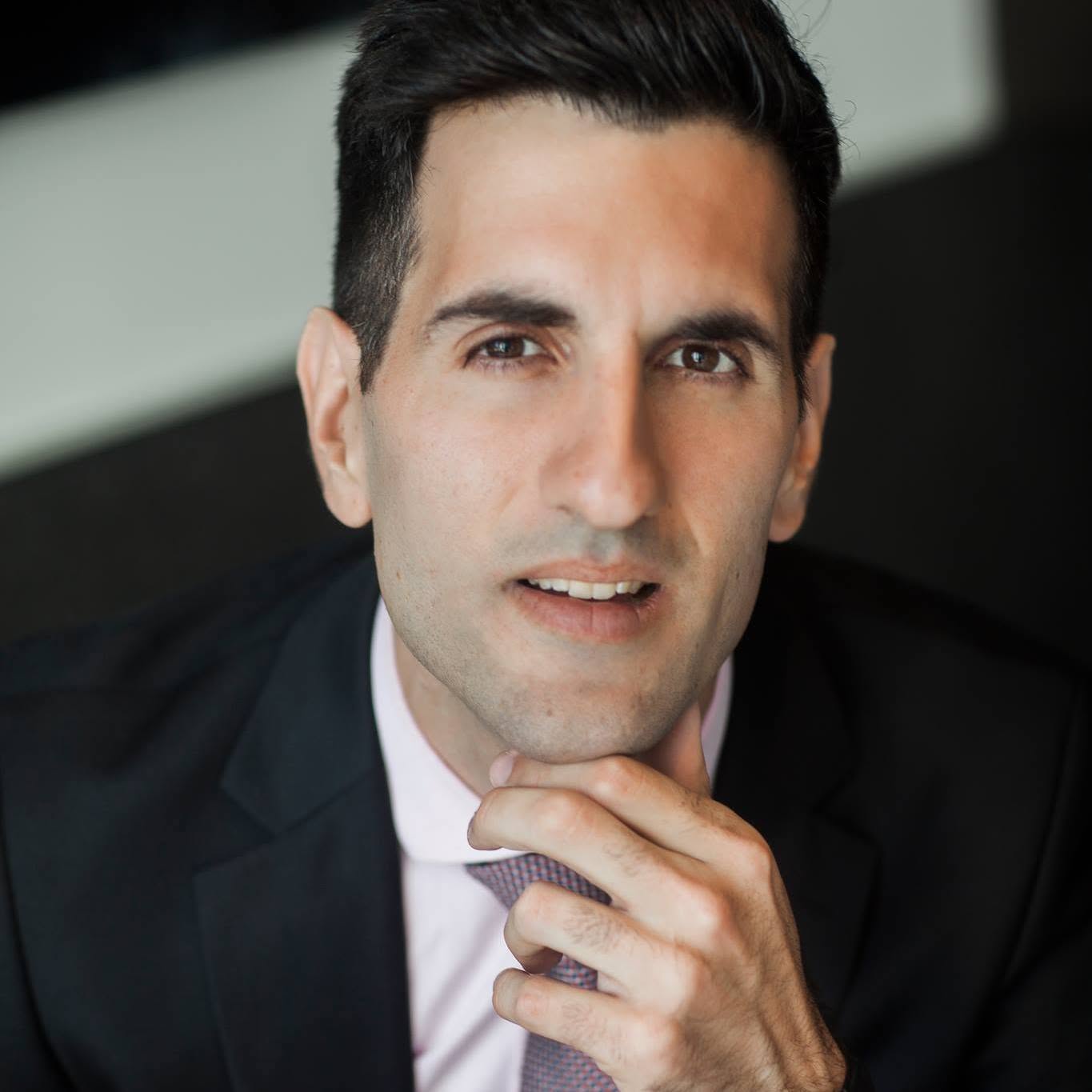 Head-and-shoulders portrait of Paul Salvatori, short dark hair, wearing a dark suit, light pink shirt, and patterned tie.