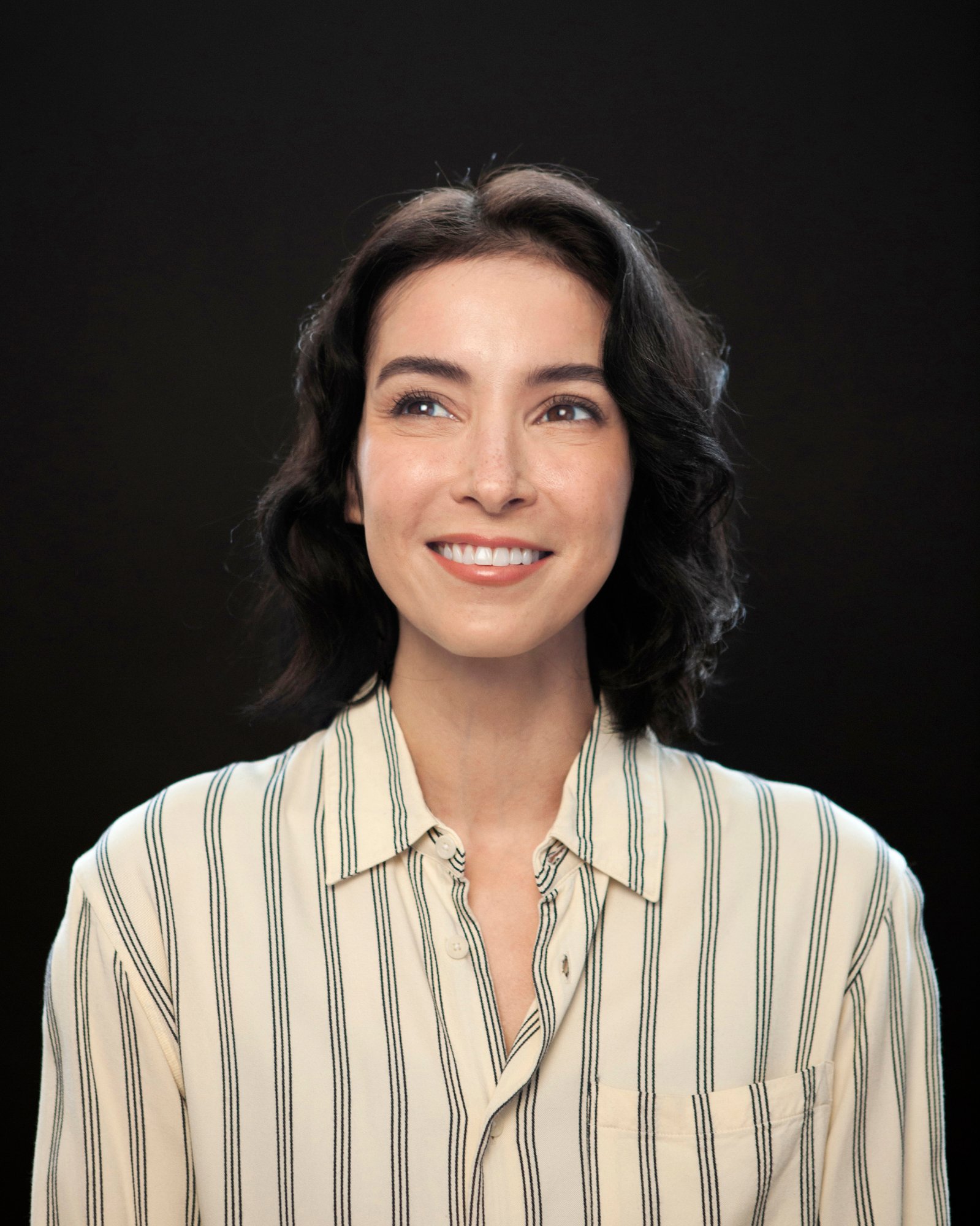 Head-and-shoulders portrait of Diana Chan McNally, shoulder-length dark curly hair, wearing a striped button-up shirt.