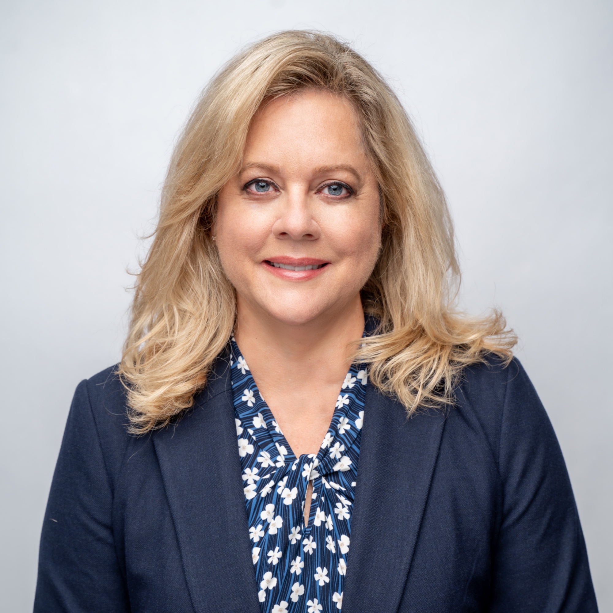 Head-and-shoulders portrait of Sabrina Zuniga, shoulder-length blonde hair, wearing a navy blazer and floral top.