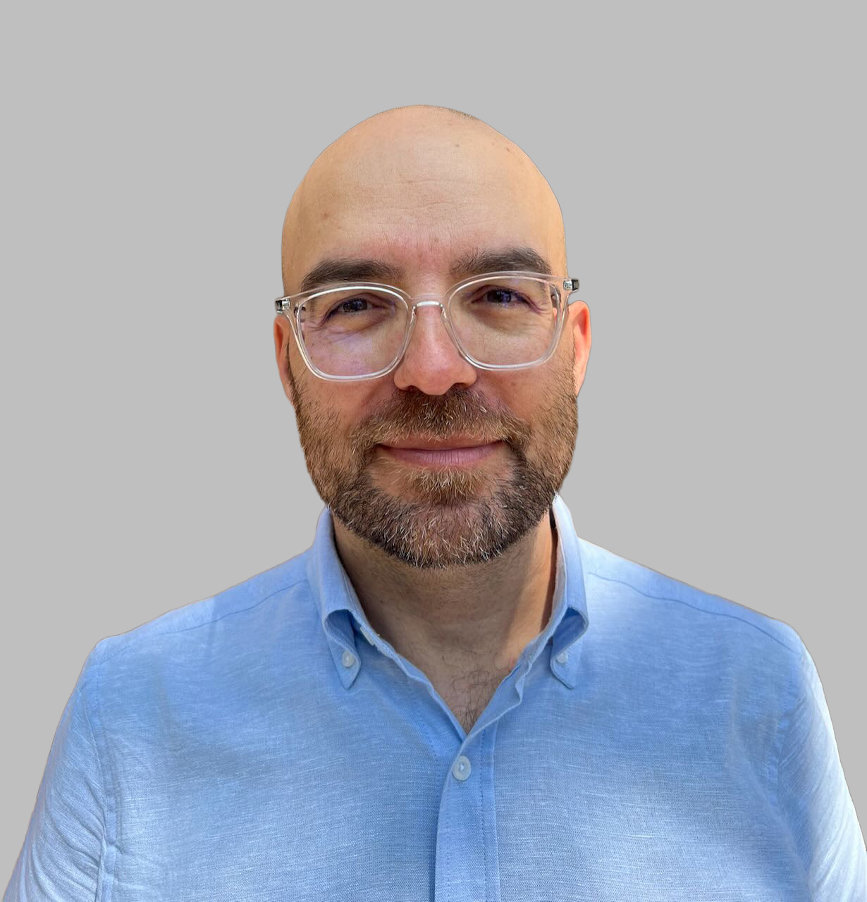 Head-and-shoulders portrait of Gian Pileri, bald, with a beard, wearing clear-framed glasses and a light blue shirt.