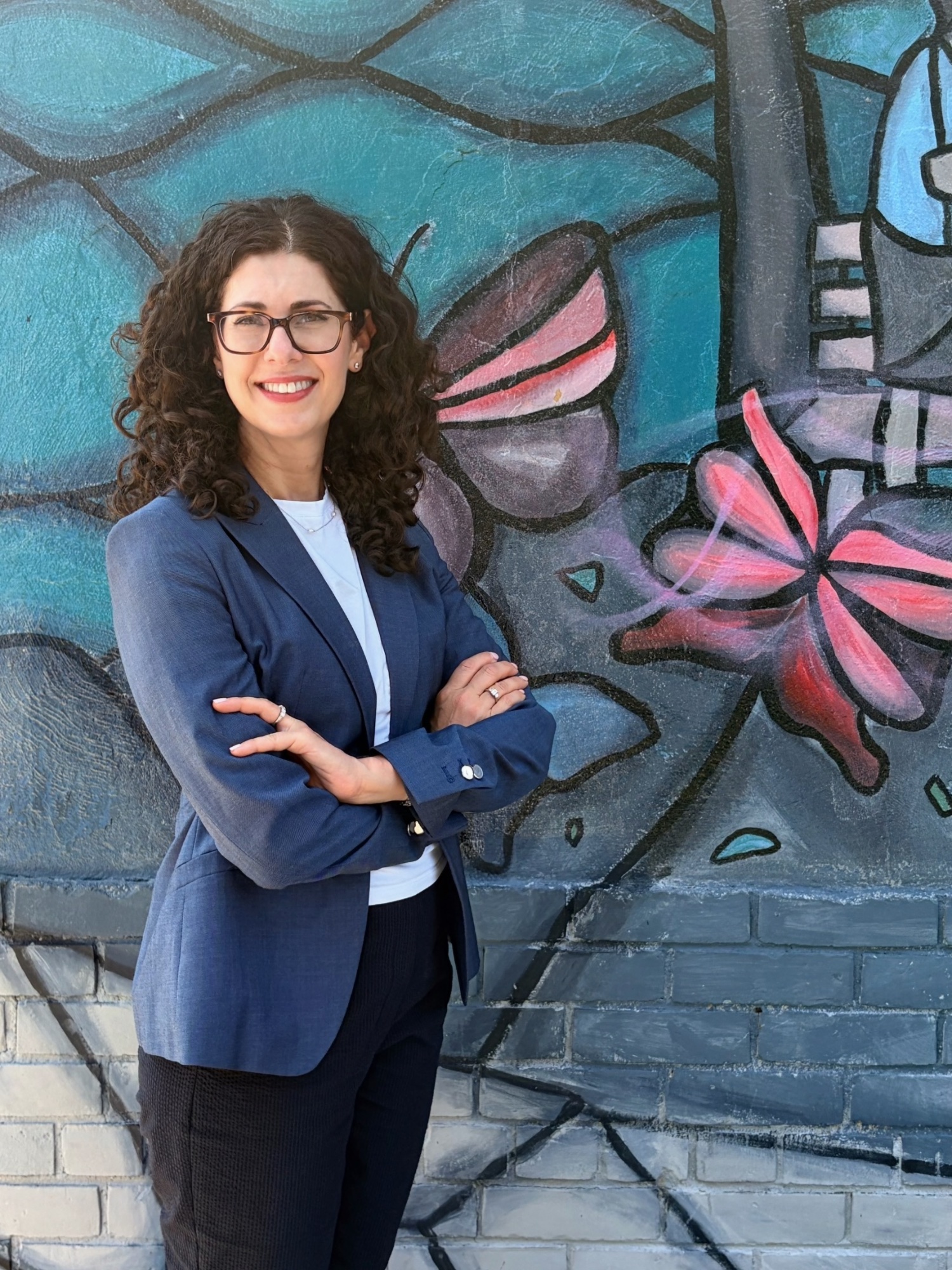 Head-and-shoulders portrait of Stacey Cline, curly dark hair, wearing glasses and a navy blazer.