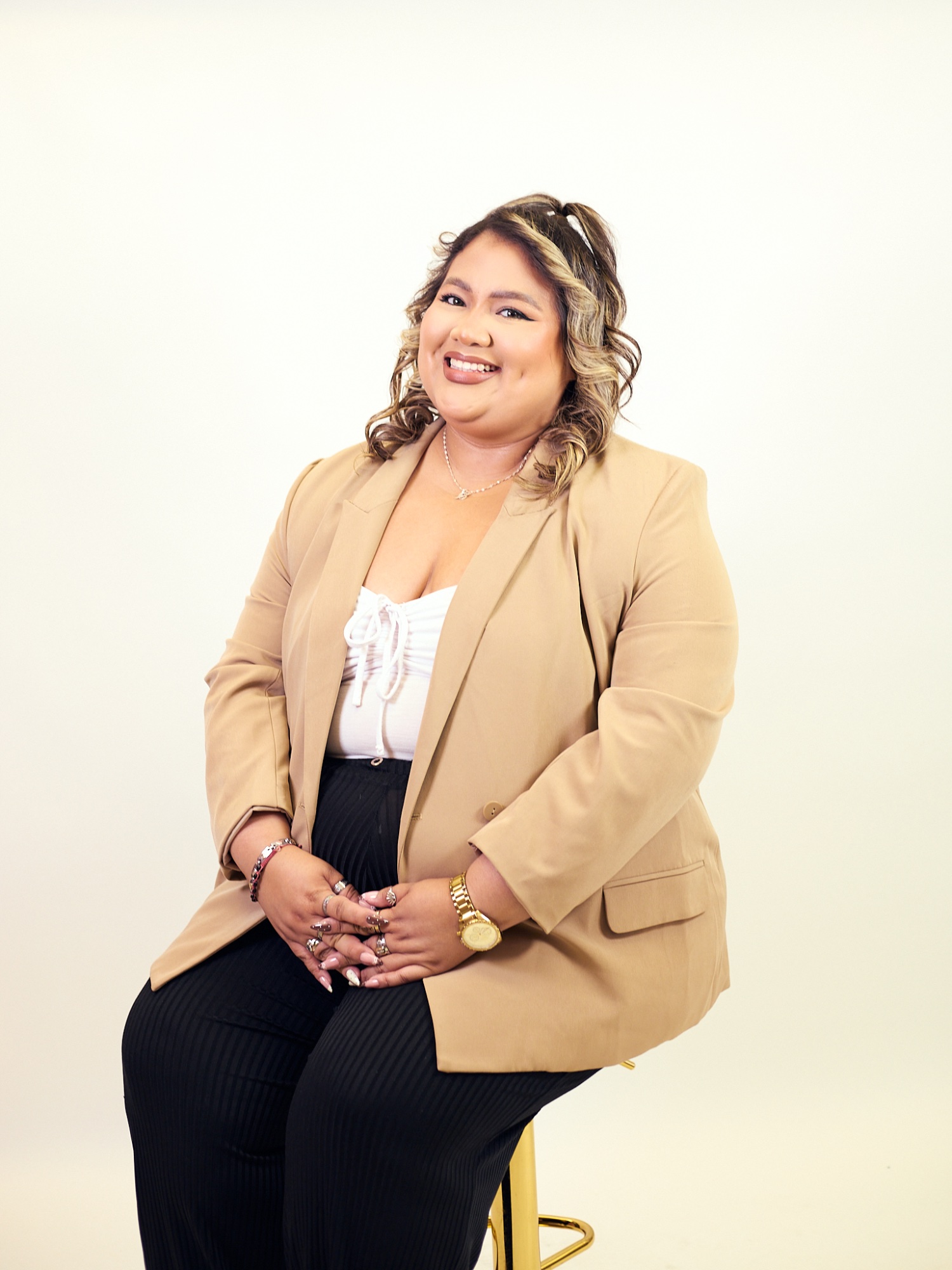 Head-and-shoulders portrait of Stephanie Loor Ruiz, curly dark hair with highlights, wearing a tan blazer over a white top.