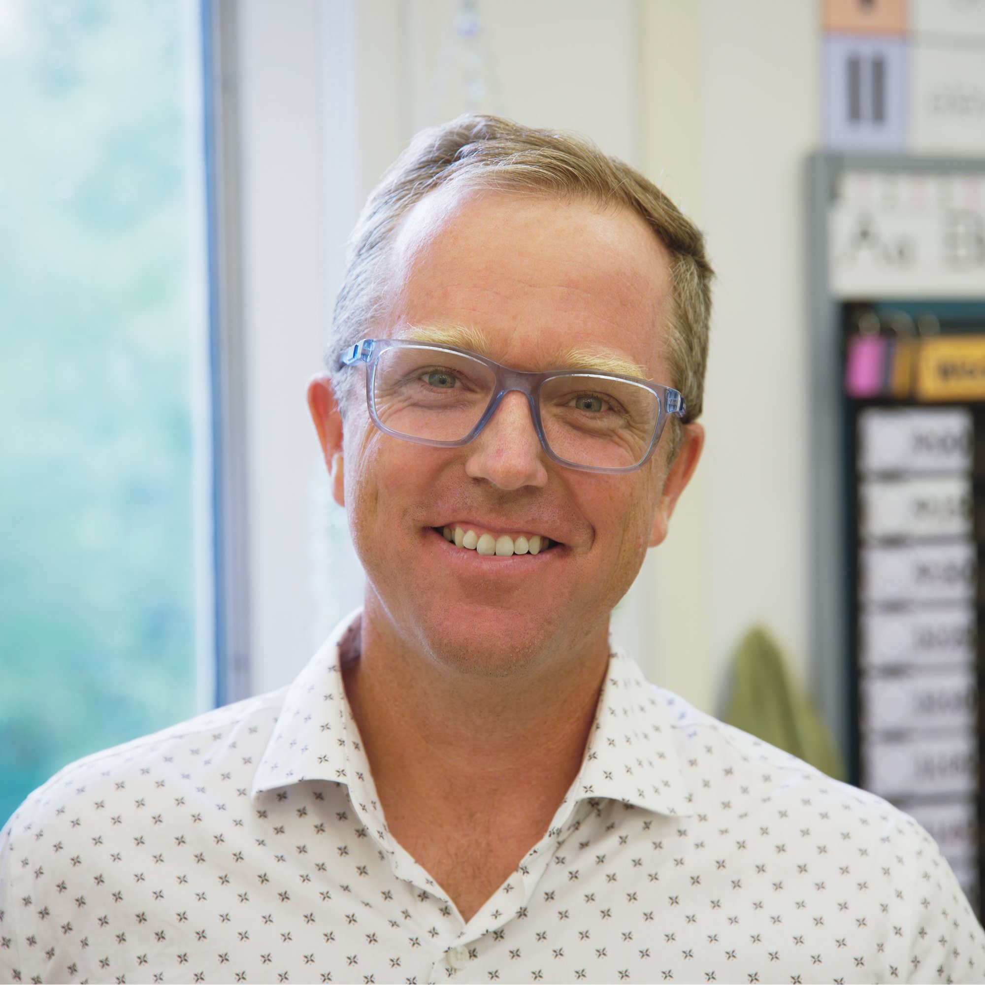 Head-and-shoulders portrait of Jared Kolb, short brown hair, wearing glasses and a white patterned shirt.