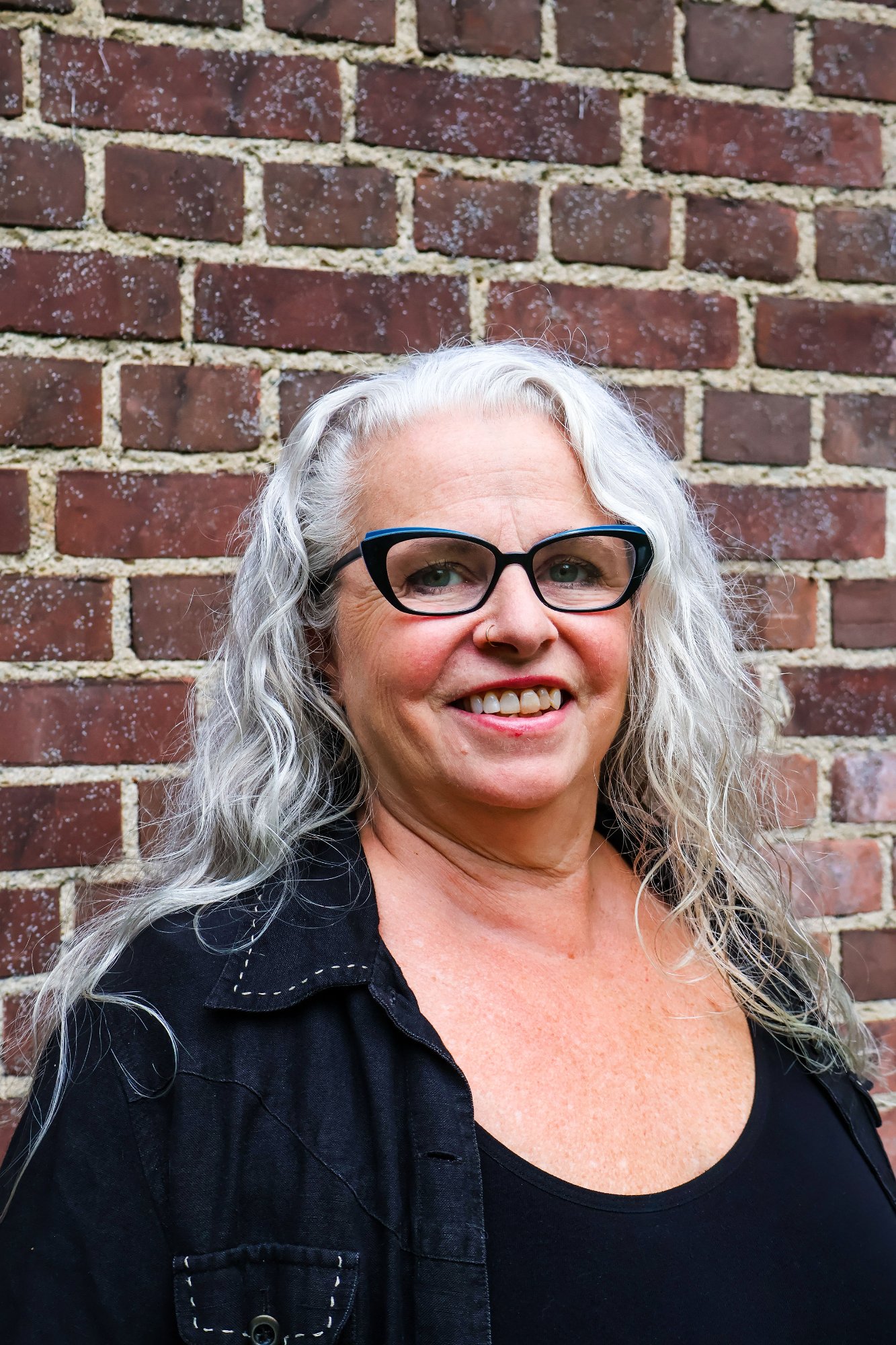 Head-and-shoulders portrait of Karen Emerson, long white hair, wearing a black top and glasses.