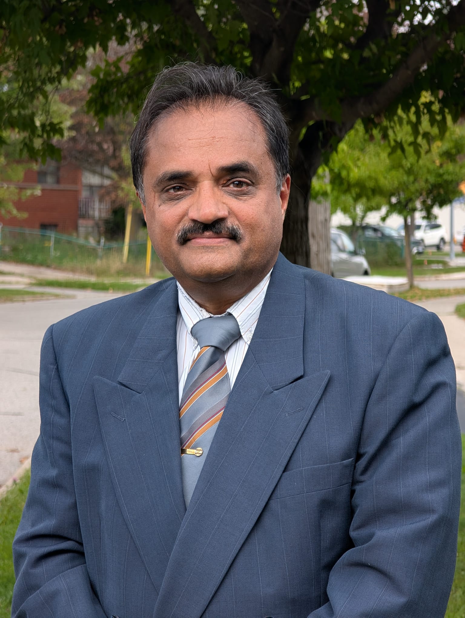 Head-and-shoulders portrait of Ketan Purohit, short grey and dark hair and a moustache, wearing a navy suit, striped shirt, and grey striped tie.