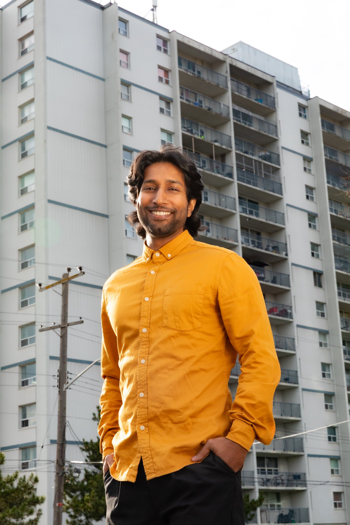 Head-and-shoulders portrait of Krissan Veerasingam, dark shoulder-length hair and a beard, wearing a mustard shirt.