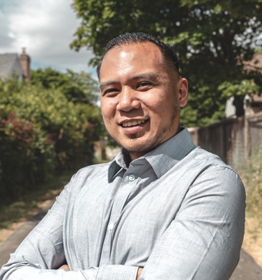 Head-and-shoulders portrait of Kristian Santos, short dark hair and a goatee, wearing a light grey button-up shirt.