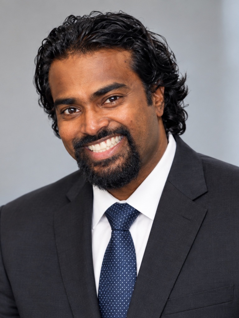 Head-and-shoulders portrait of Vimuththan Nantheeswarar, curly dark hair and a beard, wearing a dark suit and tie.