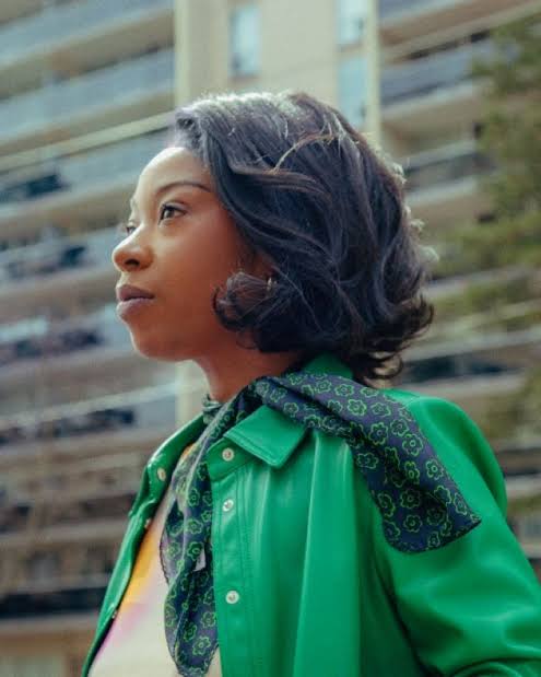Head-and-shoulders portrait of Chloe Brown, shoulder-length dark curly hair, wearing a green jacket and a patterned scarf.