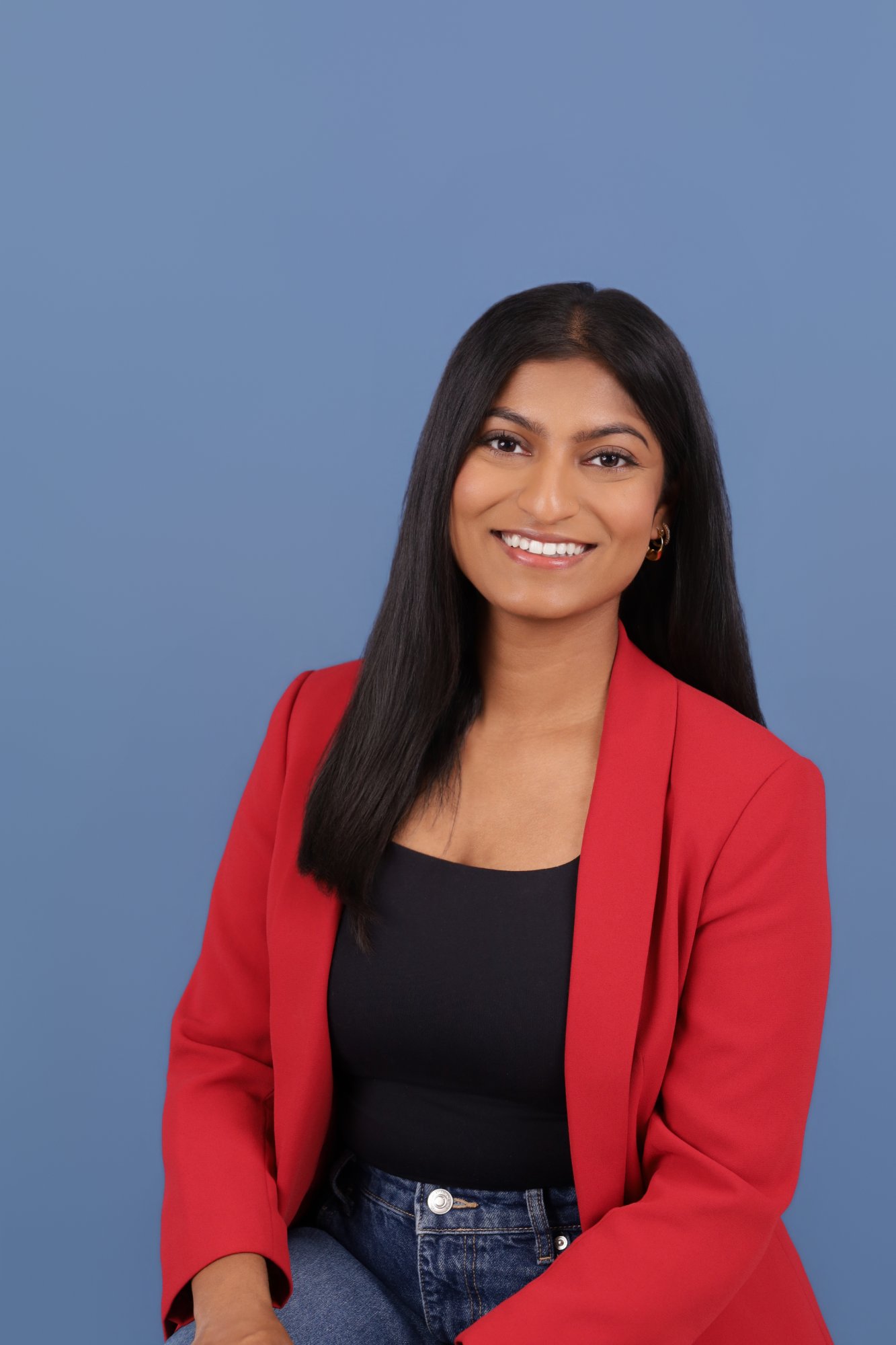 Head-and-shoulders portrait of Ravicha Ravinthiran, long dark hair, wearing a red blazer over a black top.